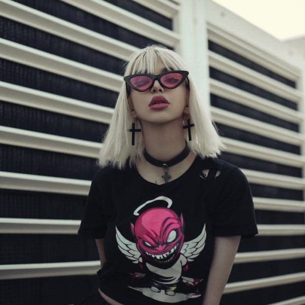 Portrait of a woman in grunge fashion style with gothic accessories, pink eyeglasses, and a graphic tee.